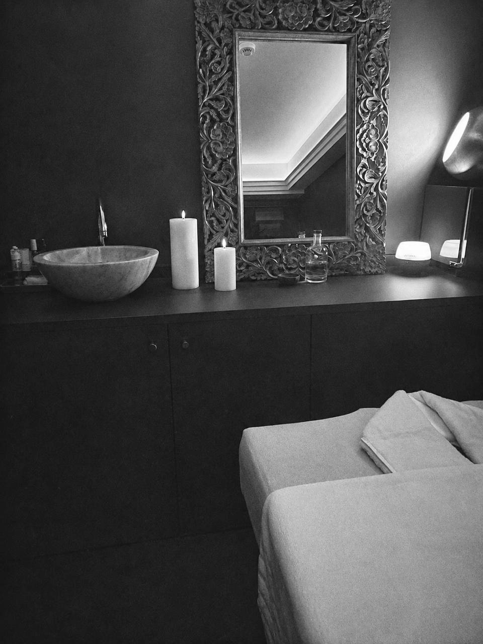 La cabine de soin : un miroir sculpté, des bougies et une vasque en marbre.